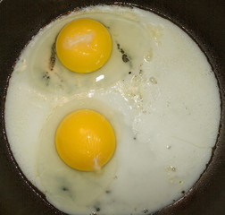 Two fried eggs in a non-stick frying pan sunny side up.