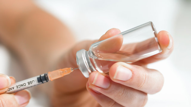 Macro image of female doctor's hands holding ampule with medication and filling syringe