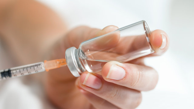 Macro image of female hands holding small syringe and glass ampule with medication