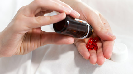 Closeup photo of young woman shaking bottle with pills and pouring them on hand