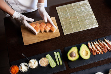 Closeup view of process of preparing rolling sushi. Master is serving fresh delicious rolls on the wooden board