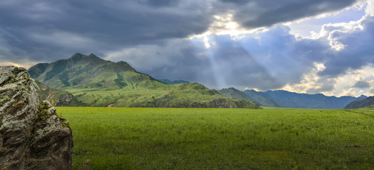 Fototapeta na wymiar Sunbeams shining through the clouds over mountain ranges and valley - panoramic view