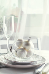 Silver and white Christmas Table Setting with christmas decorations above light window