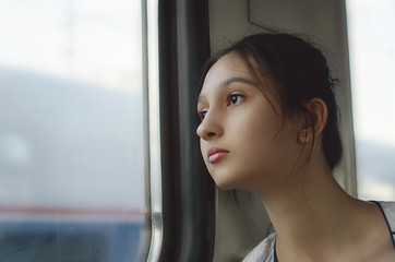 Fototapeta na wymiar A cute girl travels by train and looks out the window.