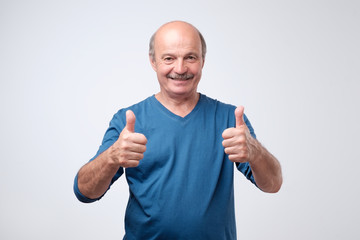 Handsome senior man in blue shirt shows thumb up. He is satisfied with advice