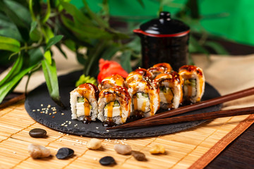 Sushi rools with cheese, eel and cucumber decorated with teriyaki sauce served with sticks at green background.