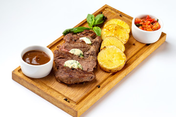 Wooden board with roast beef meat served with fried potatoes and tomato sauce isolated at white background.