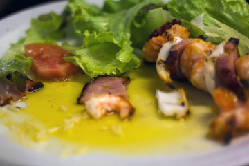 Squid and prawn skewers on a plate with sauce and salad