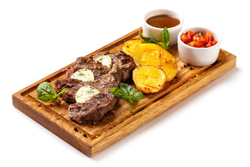 Wooden board with roast beef meat served with fried potatoes and tomato sauce isolated at white background.