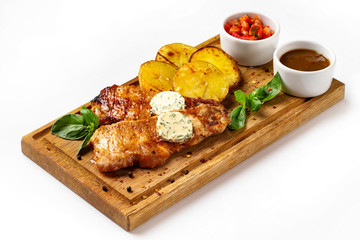 Wooden board with roast pork meat served with fried potatoes and tomato sauce isolated at white background.