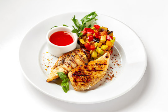 Plate with fried chicken breast served with ratatouille vegetables and tomato sauce isolated at white background.