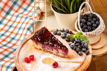 Slice of bilberry cheese cake served with sugar powder at decorated table background.
