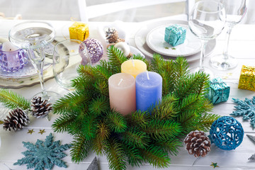 Festive decoration on Christmas table setting with candles, lantern, tableware and wine glasses on white wooden background