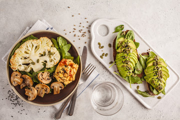Cauliflower steak with grilled champignons and hummus and avocado toast, top view.