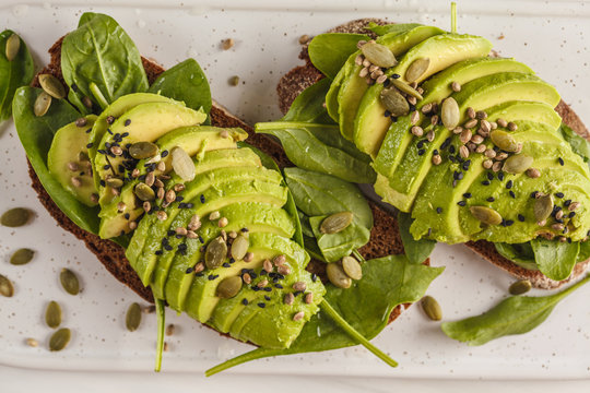 Avocado toast with hemp seeds, sesame seeds and pumpkin seeds on a white marble board, top view.