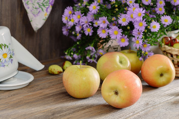 Ripe ruddy apples on a wooden table next to a bouquet of flowers