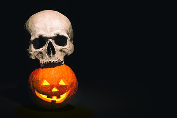 Halloween scene. Human skull on Halloween pumpkin on dark black background. Free space for your...