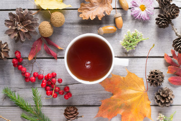 Cup of tea, autumn leaves, berries, cones on wooden background