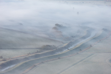 Stunning foggy English rural landscape at sunrise in Winter with layers rolling through the fields