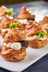 Savory profiteroles with different types of fillings. Salty cakes for snacks. Mini sandwiches, canapes with vegetables, meat, liver, sauce. An exquisite French snack for a buffet at the feast.