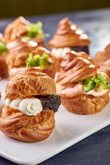Savory profiteroles with different types of fillings. Salty cakes for snacks. Mini sandwiches, canapes with vegetables, meat, liver, sauce. An exquisite French snack for a buffet at the feast.