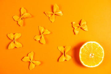 Creative summer layout made of oranges and colored pasta semolina papillon on bright orange background. Fruit minimal concept