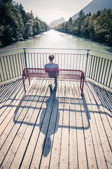 Junge Frau sitzt entspannt auf Spazierbank, Blick auf Fluss und Wälder