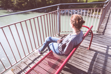 Junge Frau sitzt entspannt auf Spazierbank, Blick auf Fluss und Wälder