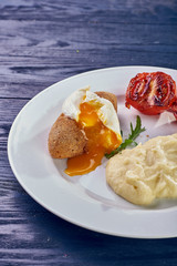 A full-fledged hot dinner on a white plate in a cafe, restaurant. Chicken Kiev stuffed with breaded, poached eggs, grilled tomato, arugula and mashed potatoes for dinner.