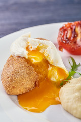 A full-fledged hot dinner on a white plate in a cafe, restaurant. Chicken Kiev stuffed with breaded, poached eggs, grilled tomato, arugula and mashed potatoes for dinner.