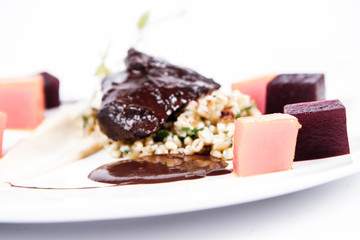 Beef cheeks with vegetables, roasted parsley root mousse , pearl barley, dark chocolate and demi glace sauce on a white background