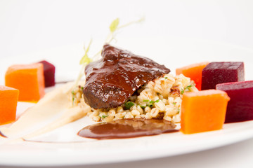 Beef cheeks with vegetables, roasted parsley root mousse , pearl barley, dark chocolate and demi glace sauce on a white background