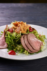 A hearty nice salad for the festive table. Slices of salted meat, bacon, beef, veal, pork from oven, meat sausage, ham. Appetizer from greenery, arugula, mushrooms chanterelles and cherry tomatoes.