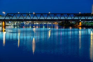 Railroad bridge over river Weser at night with train rushing by and Bremen city center in background