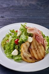 Expensive Italian, Spanish, French salad for festive table. Snack from pear, mozzarella, jamon, greens, lettuce, sauce. Cuisine of France, Spain, Italy. Photo of food for menu, cookbook, culinary blog