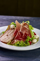 Expensive Italian, Spanish, French salad for festive table. Snack from pear, mozzarella, jamon, greens, lettuce, sauce. Cuisine of France, Spain, Italy. Photo of food for menu, cookbook, culinary blog