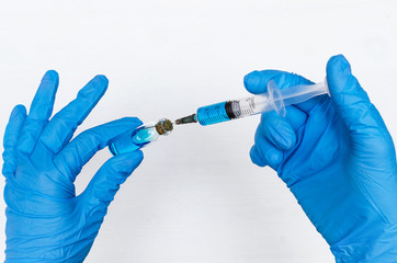 Nurse is holding in hand a syringe with blue liquid drug on the doctor table background.