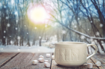 Cup of coffee or cocoa on a wooden table in a winter forest
