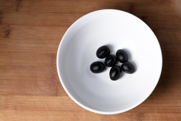 Black olives in bowl from above view on wooden plate background