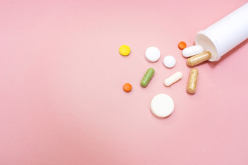 Tablets and pills from a bottle on a pink background
