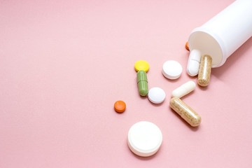 Tablets and pills from a bottle on a pink background