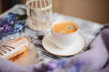 Obraz na płótnie Canvas Cup of hot coffee, eclair and flowers on rustic wooden table, closeup photo warm sweater, winter morning concept, top view. Vintage tinted