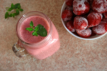  Smoothie with frozen strawberries and natural yoghurt decorated with a sprig of mint, frozen strawberries in a bowl