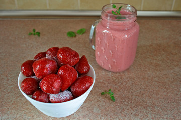 Smoothie with frozen strawberries and natural yoghurt decorated with a sprig of mint, frozen strawberries in a bowl