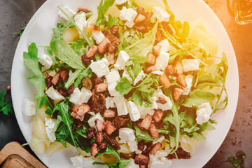 Top view of a plate with food. A dish of pasta, rucola and spices, next to the ingredients of food, garlic, tomatoes on a stone, dark countertop. The concept of preparing food.