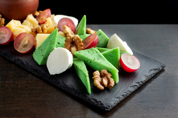 Cheese plate on black shale. Pieces of fruit.