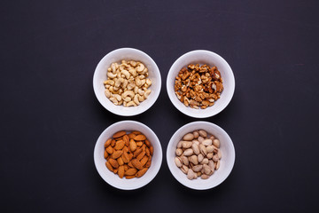 Four bowls with different nuts on a black table