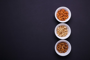 Three bowls with different nuts on a black table
