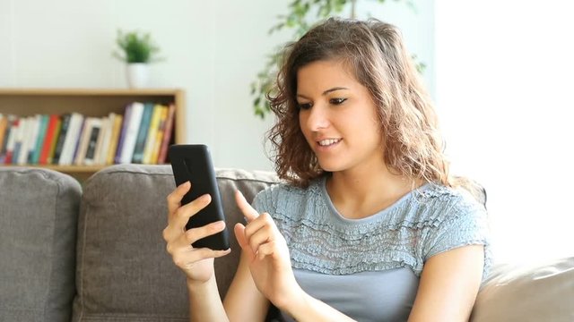 Happy woman using a mobile phone sitting on a couch at home