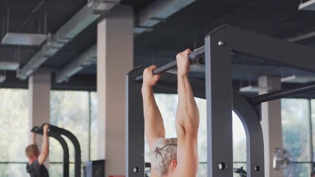 Strong blonde man doing pull ups on horizontal bar. Chin-ups in the gym
